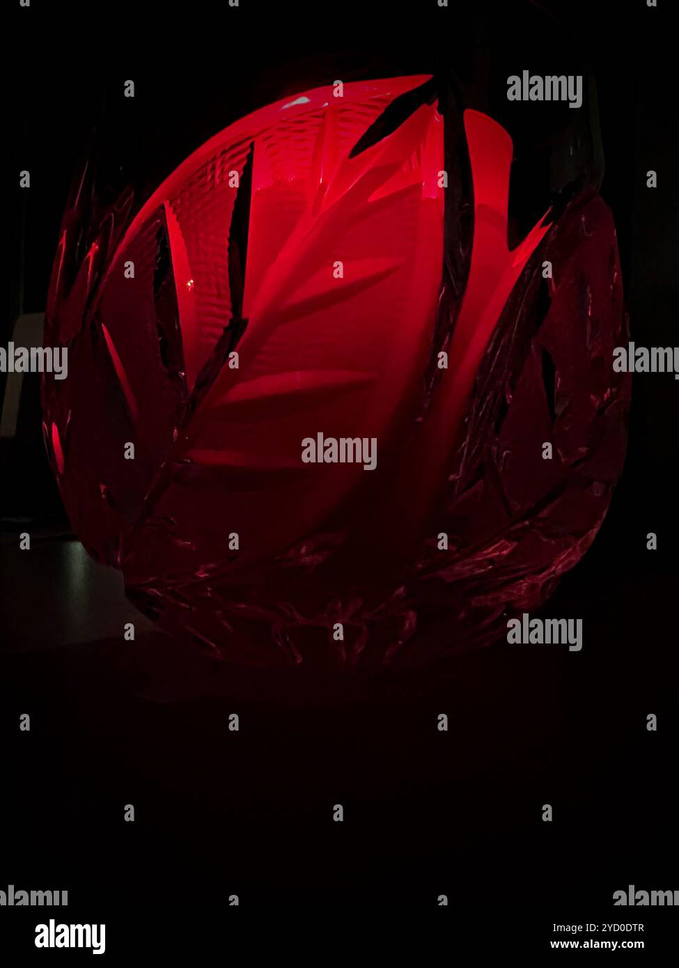 Un bagliore rosso cremisi proveniente da una ciotola di cristallo intagliata, che illumina l'oscurità con un inquietante spirito di Halloween. - Immagine stock catturata con smartphone