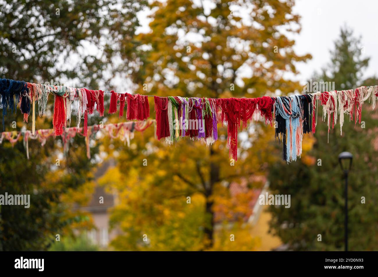 Installazione di filati riciclati appesi sopra la strada. Decorazioni esterne sospese in filato di lana. Sfondo autunnale. Foto Stock