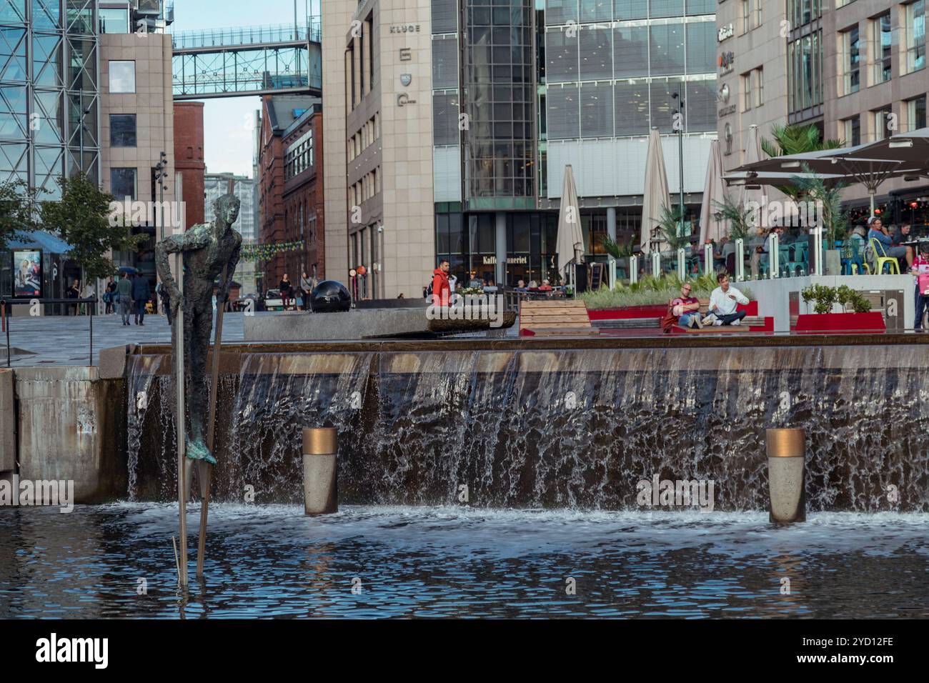 Oslo, Norvegia - 18 agosto 2018: Scultura in acqua presso Aker Brygge, Oslo con persone che si rilassano su una panchina durante il giorno Foto Stock
