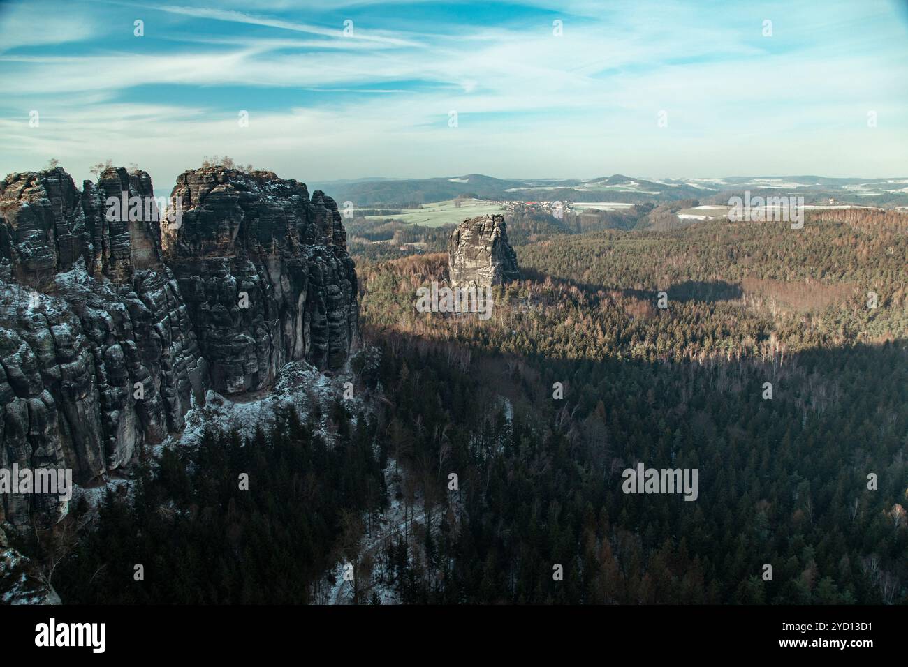 Una vista mozzafiato cattura le spettacolari scogliere delle Badlands nella Sassonia svizzera, circondate da una fitta foresta coperta di neve sotto un sole luminoso Foto Stock