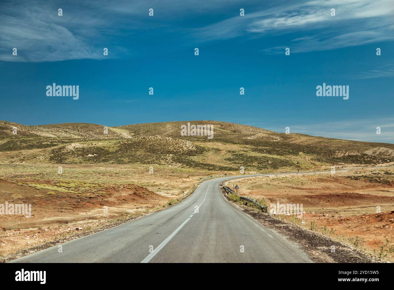 Una tortuosa strada sterrata si estende attraverso i calanchi del Marocco, circondati da un vasto paesaggio di colline e praterie sotto un cielo blu brillante. Il terr Foto Stock