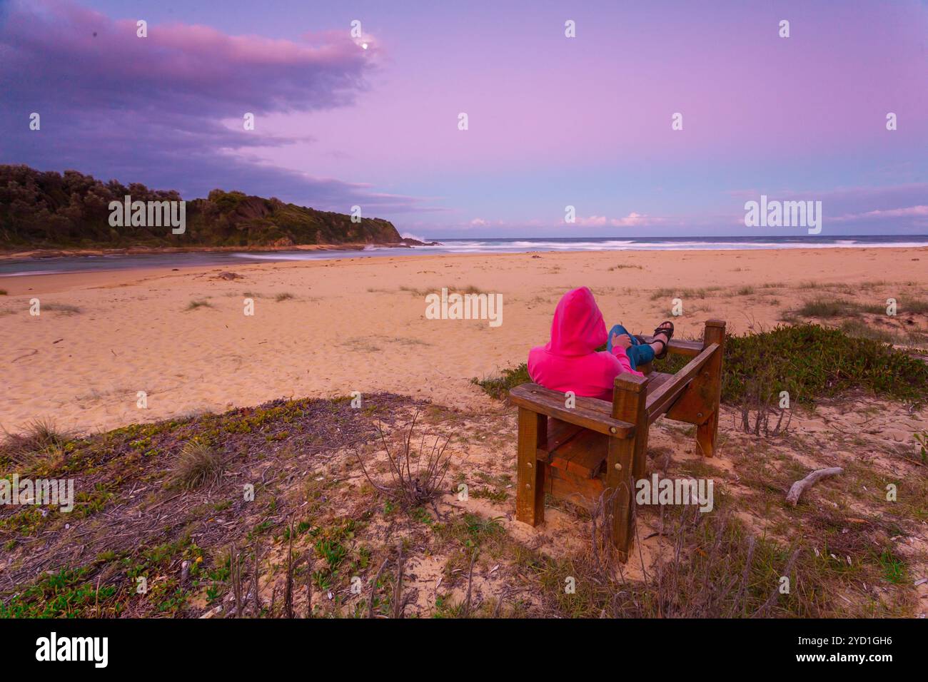 La donna si rilassa sulla panchina affacciata sulla spiaggia al tramonto del pomeriggio Foto Stock