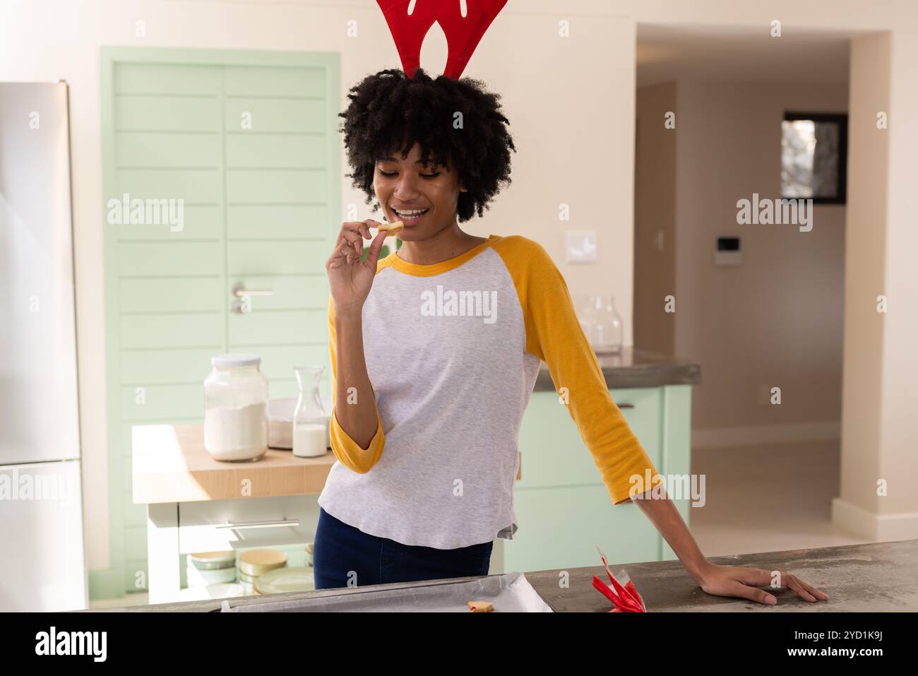 Donna che indossa corna di renna che si gusta i biscotti di Natale a casa Foto Stock