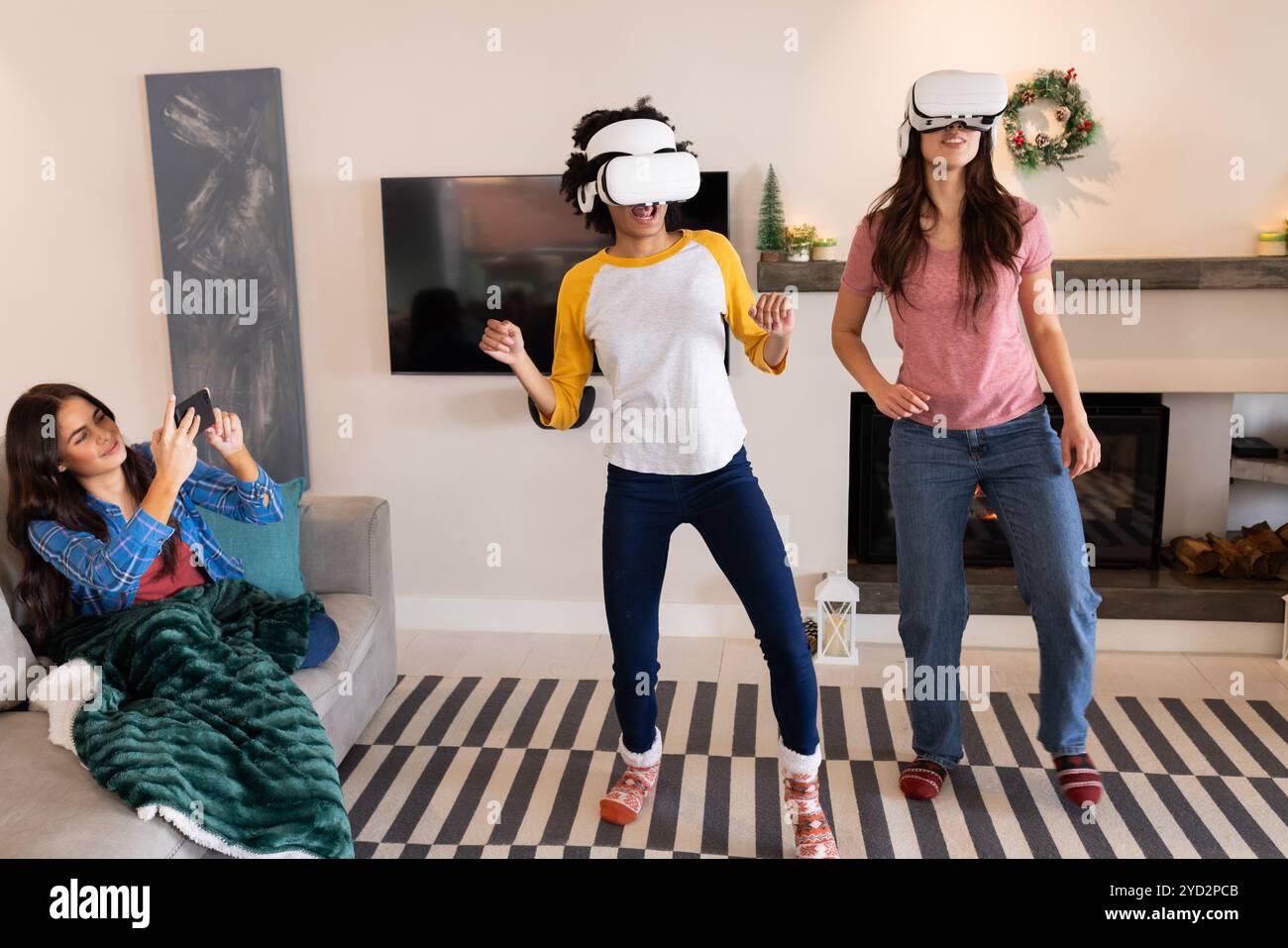Amiche mutlirazziali che si divertono a giocare in realtà virtuale a casa durante i festeggiamenti natalizi Foto Stock