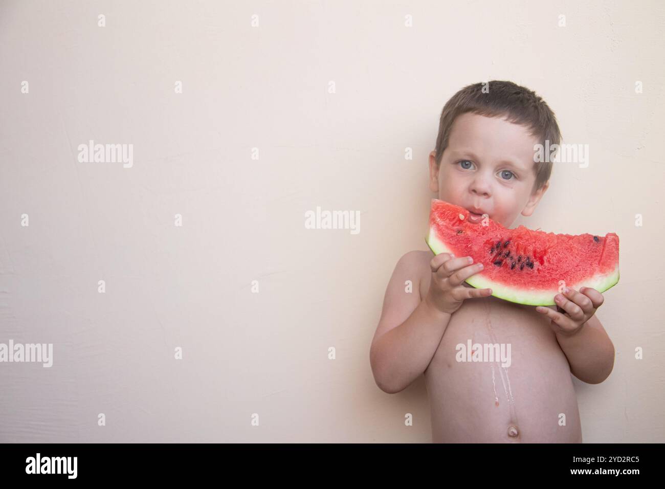 Ritratto di un ragazzo con un anguria. Un bambino felice mangia un anguria. Estate. Un ragazzo contro un muro solido con un anguria in h Foto Stock