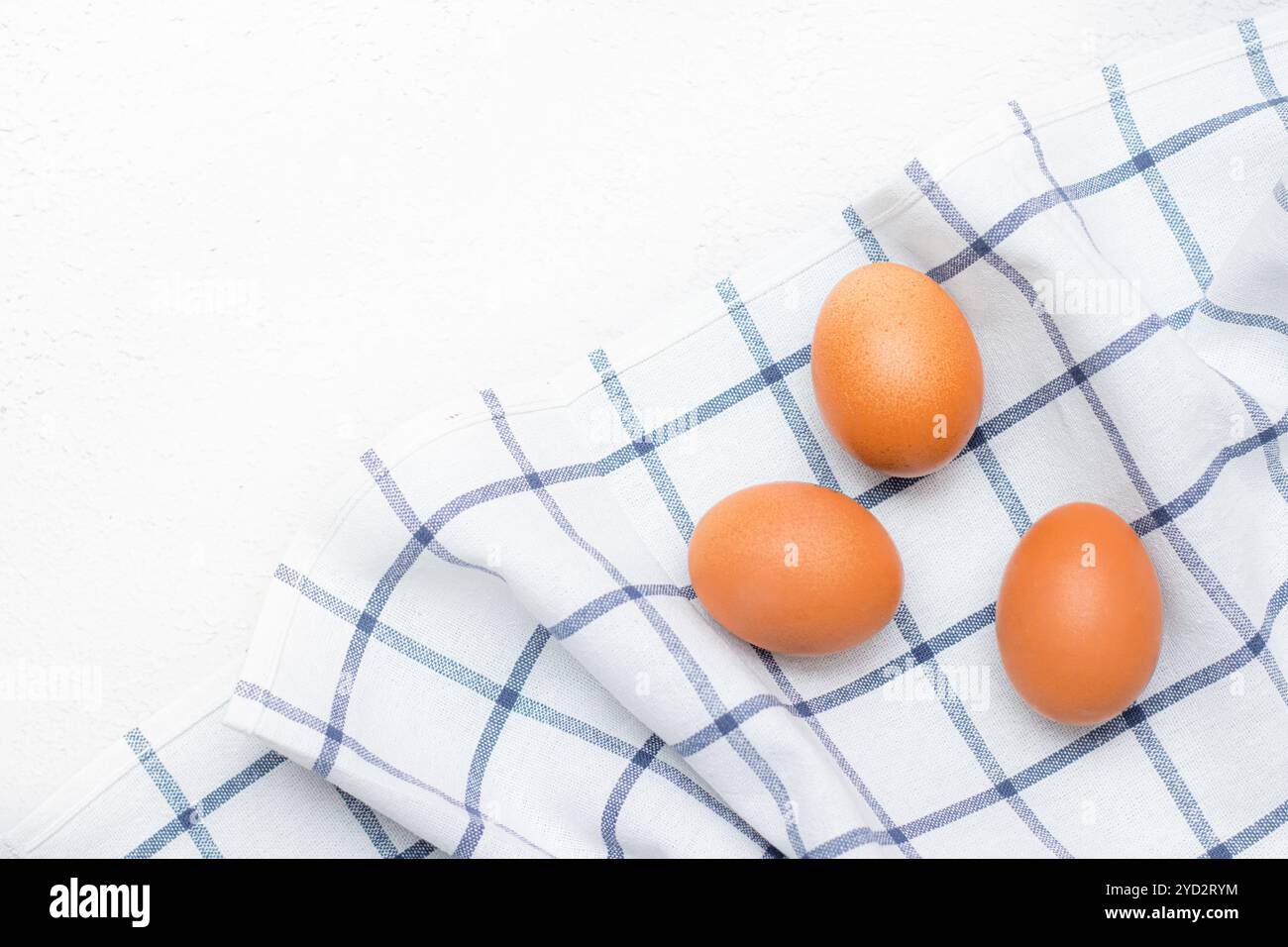 Uova di pollo su un asciugamano da cucina a quadri su un tavolo leggero. concetto di prodotti agricoli e alimenti naturali. Articolo sui prodotti per la casa Foto Stock