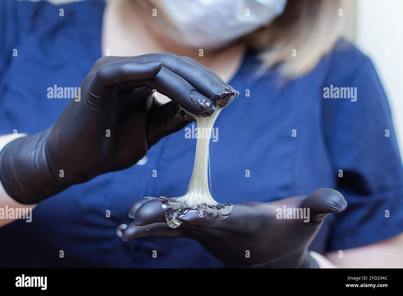 Mani femminili in guanti neri che contengono un recipiente di pasta per shugar pronto per la procedura di epilazione dello zucchero. Trattamenti spa. Beaut femminile Foto Stock