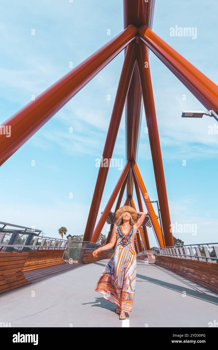 Donna sorridente spensierata che cammina con successo attraverso un moderno ponte pedonale sul fiume Foto Stock