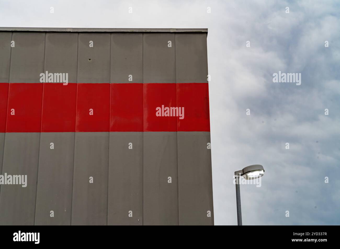 La facciata grigia dell'edificio con una striscia rossa è raffigurata sotto un cielo nuvoloso Foto Stock