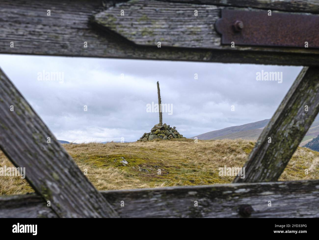 Un Cairn (pile o stack di pietre) per segnare la cima di Una collina in Scozia incorniciata attraverso Una porta di legno Foto Stock