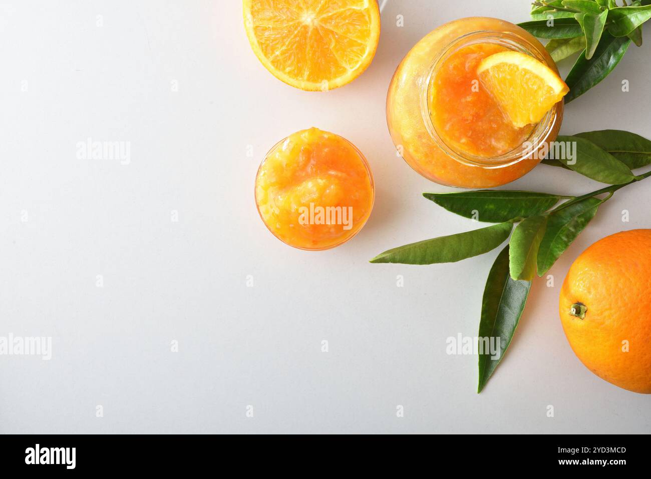 Vasi con marmellata d'arancia isolati su un tavolo bianco con frutta intorno e foglie. Vista dall'alto. Foto Stock
