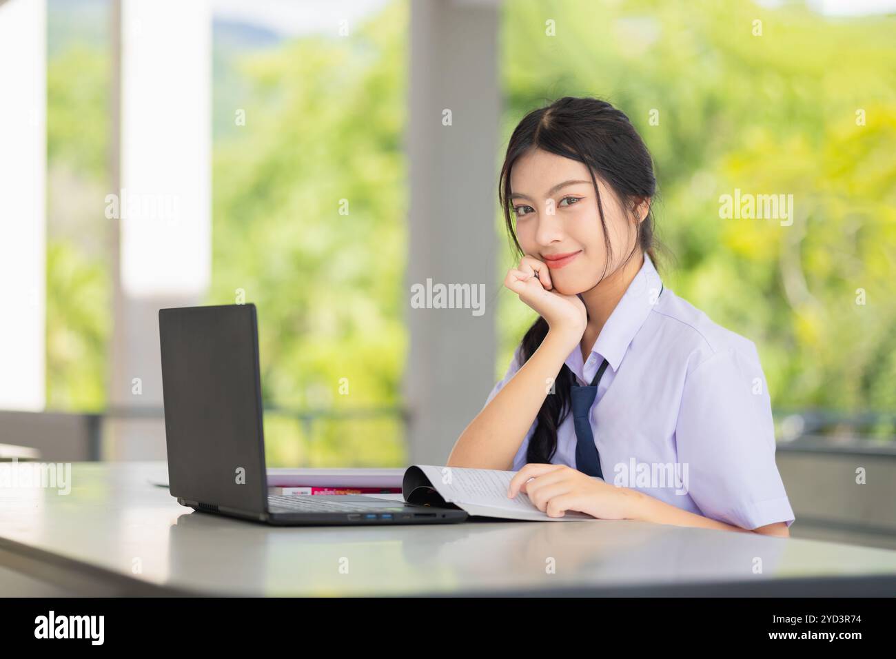 una ragazza adolescente in uniforme scolastica che usa un computer portatile per fare i compiti di apprendimento nel campus scolastico, concetto di tecnologia di autoeducazione. Foto Stock