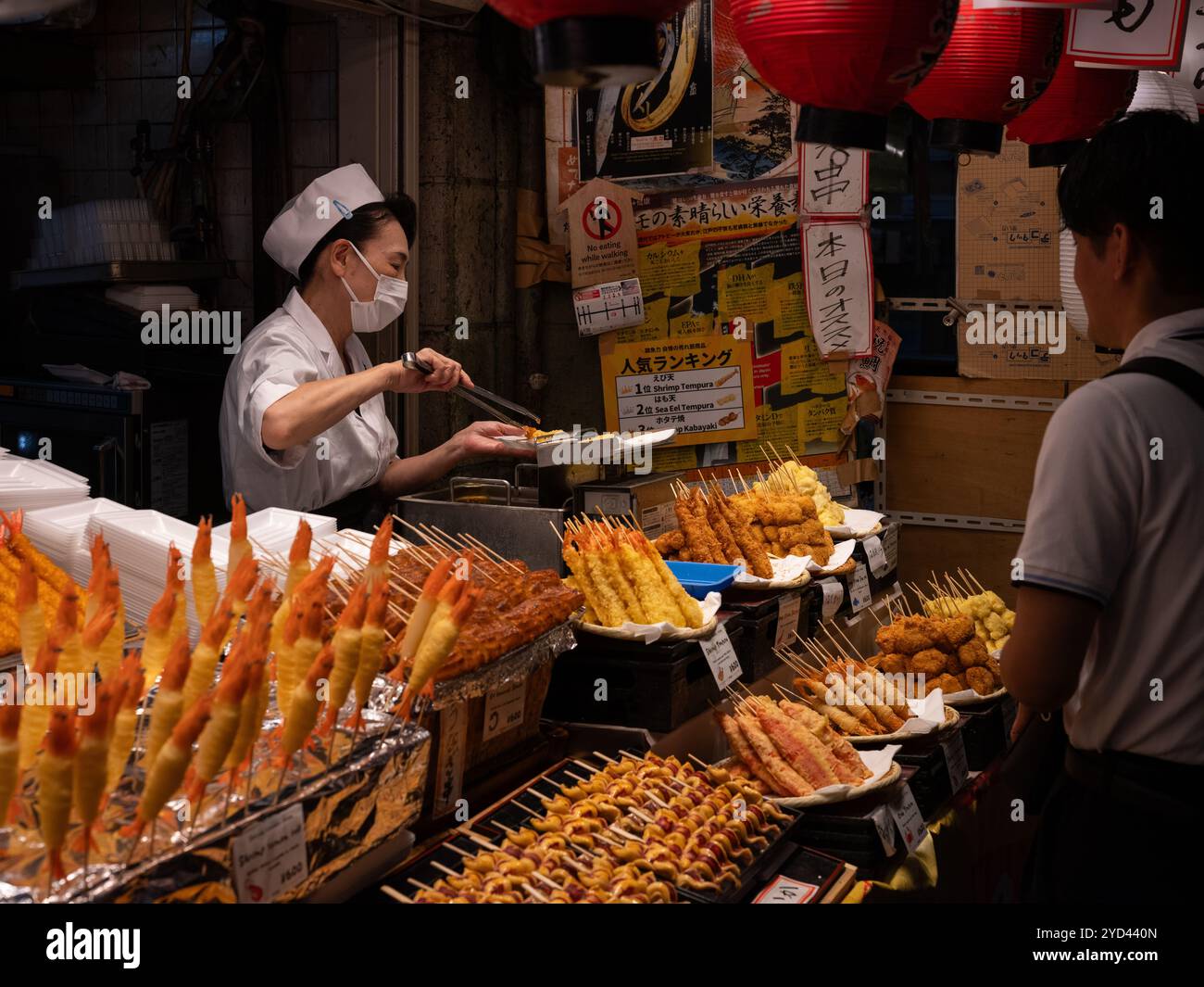 Una signora giapponese che serve cibo a un cliente nel mercato Nishiki di Kyoto, in Giappone. Foto Stock