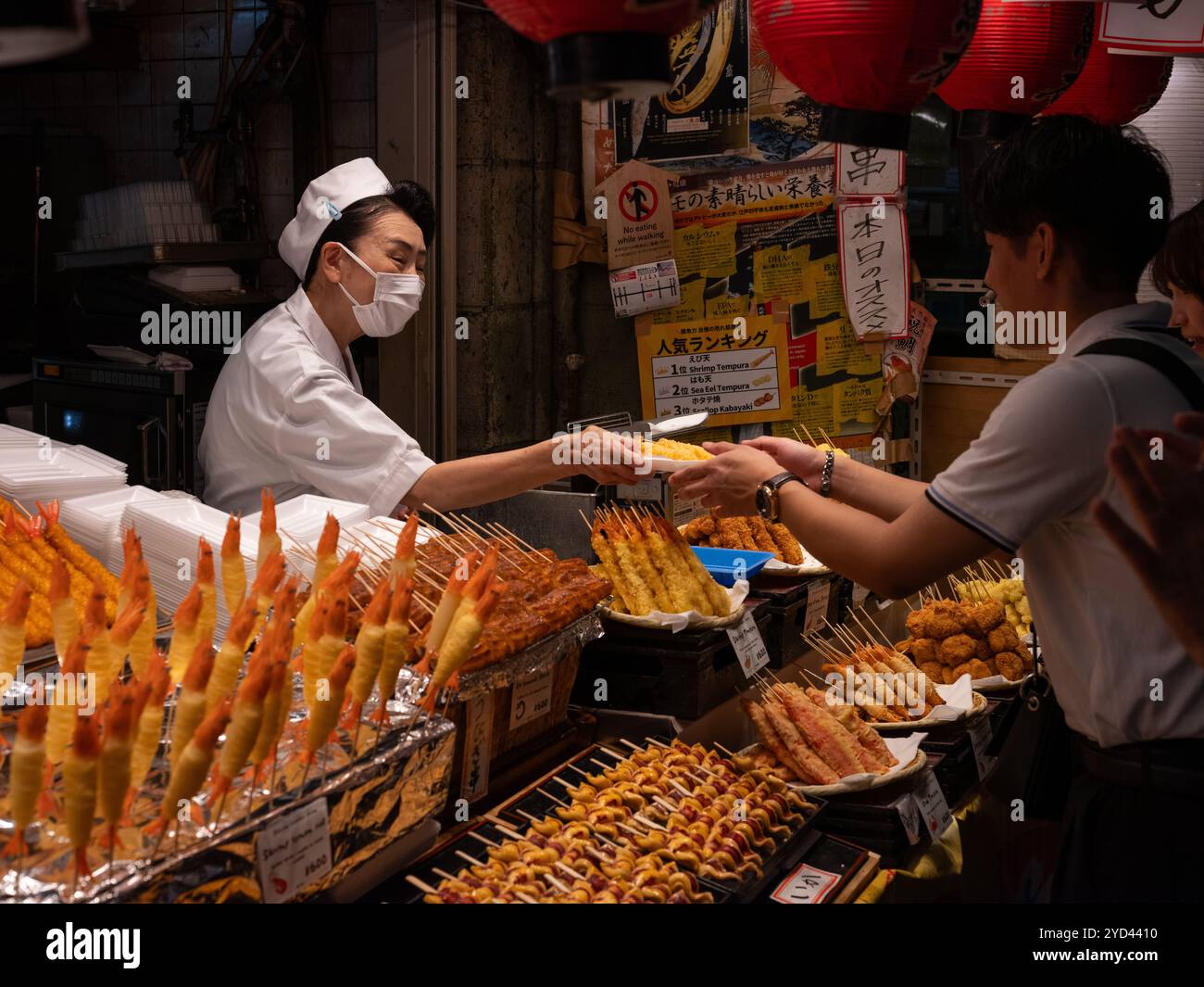 Una signora che serve cibo a un cliente nel mercato Nishiki di Kyoto, in Giappone. Foto Stock