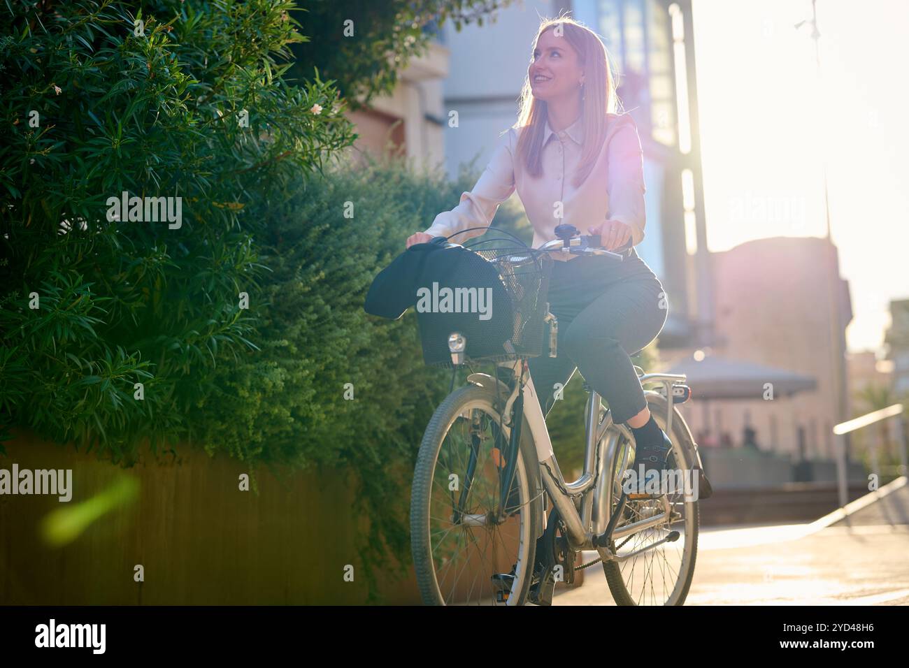 Giovane donna d'affari in bicicletta attraverso un'area urbana illuminata dal sole Foto Stock