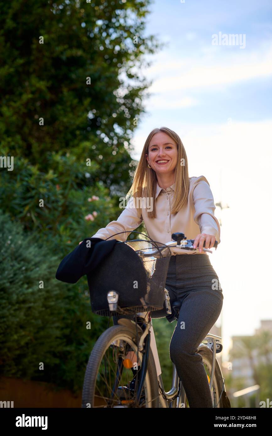 Giovane donna d'affari in bicicletta attraverso un'area urbana illuminata dal sole Foto Stock