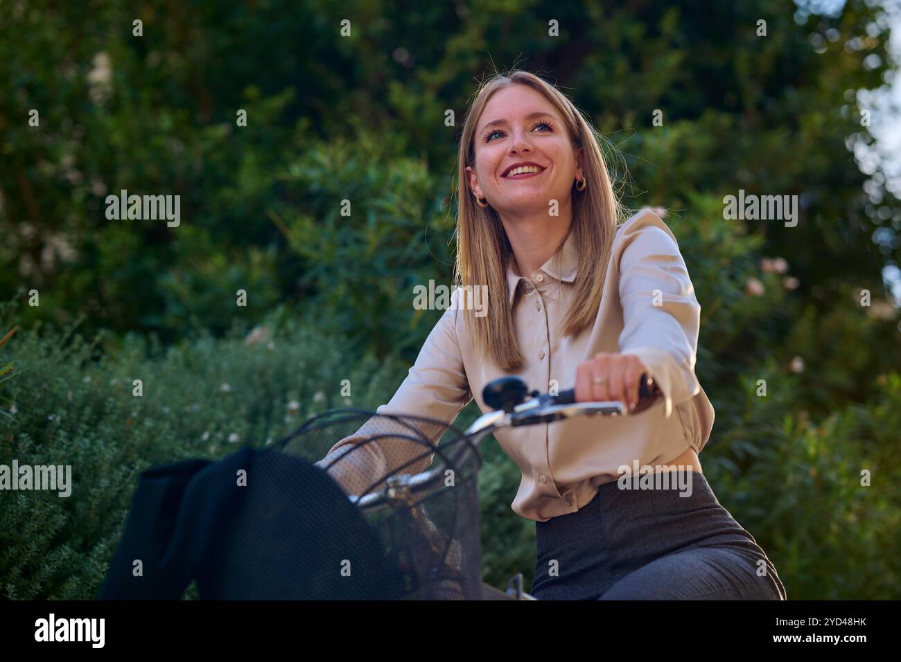 Giovane donna d'affari in bicicletta attraverso un'area urbana illuminata dal sole Foto Stock