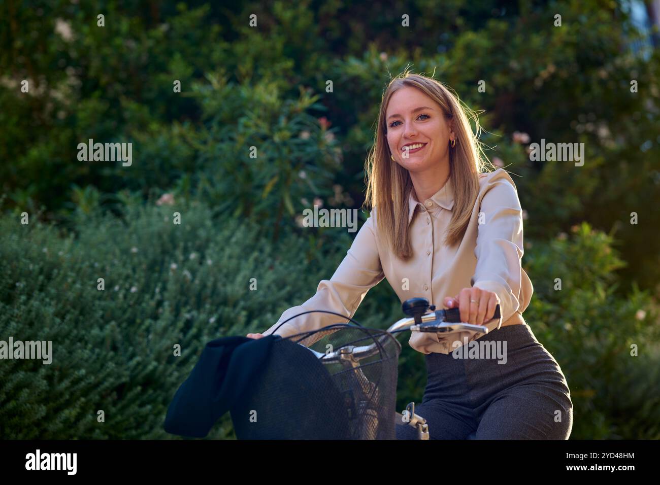 Giovane donna d'affari in bicicletta attraverso un'area urbana illuminata dal sole Foto Stock