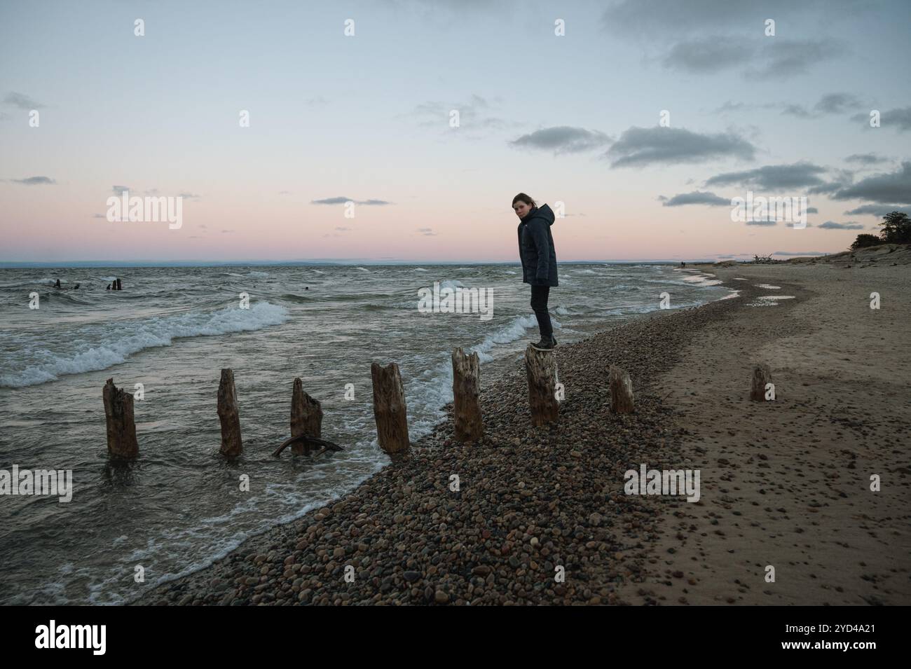 Colpo lungo di ragazzo con cappotto invernale al tramonto in equilibrio su palo di legno Foto Stock