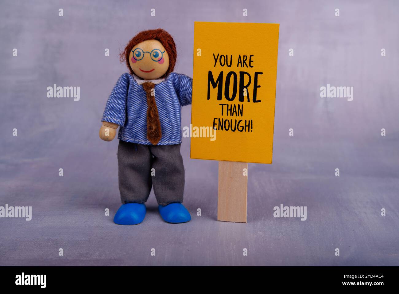 Una figura giocattolo di legno regge uno striscione giallo brillante con un messaggio motivazionale, che simboleggia la positività e l'incoraggiamento in una scena giocosa Foto Stock