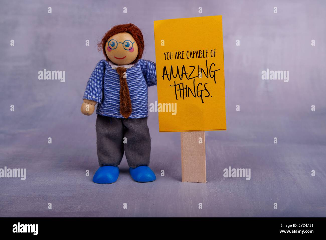 Una stravagante figura in legno presenta uno striscione giallo che mostra una citazione motivazionale, irradiando positività e ispirazione in modo giocoso Foto Stock