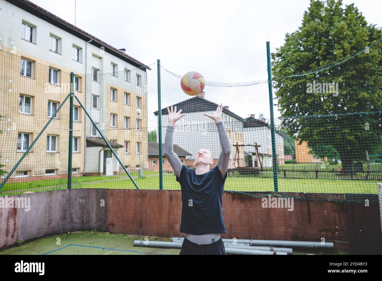 Giocatore di pallavolo che pratica l'impostazione della palla su un campo duro, concentrandosi sul controllo e la precisione durante una sessione di allenamento all'aperto. Una m calma e concentrata Foto Stock