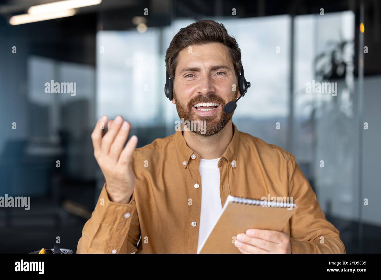 Professionista aziendale in videochiamata virtuale che dimostra capacità di comunicazione. Espressione coinvolgente, indossando l'auricolare, tenendo in mano il notebook. Ideale per i concetti di lavoro remoto, riunioni virtuali e tecnologia Foto Stock