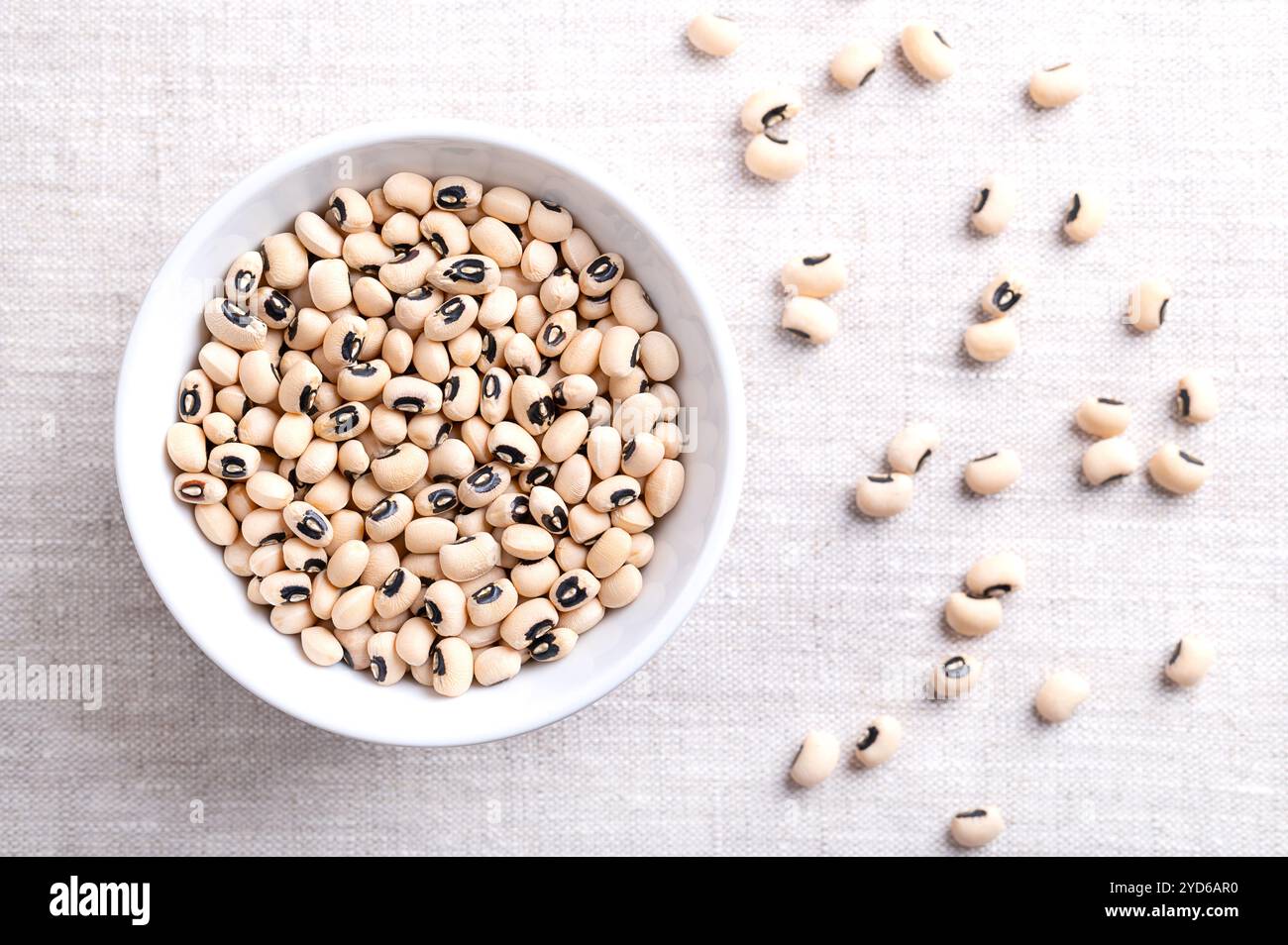 Piselli secchi dagli occhi neri in un recipiente bianco sopra il lino. Fagioli dagli occhi neri, o blackeye californiano, un legume di fagioli pallidi di medie dimensioni, con macchie nere. Foto Stock
