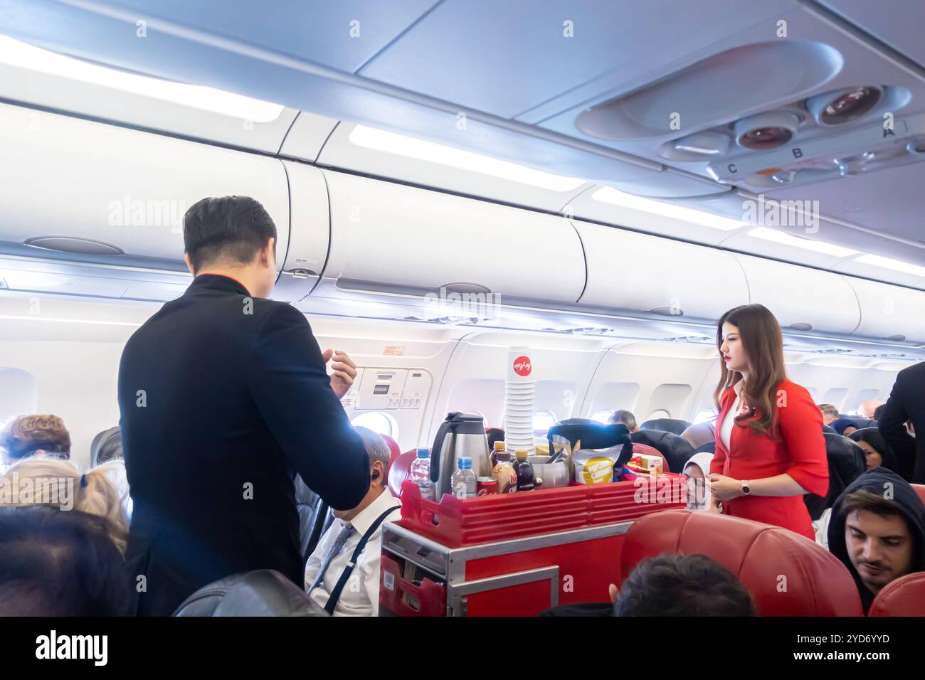 Assistenti di volo, uomini e donne, che servono cibo e bevande ai passeggeri dell'Airbus A320 operato da AirAsia Indonesia, Foto Stock