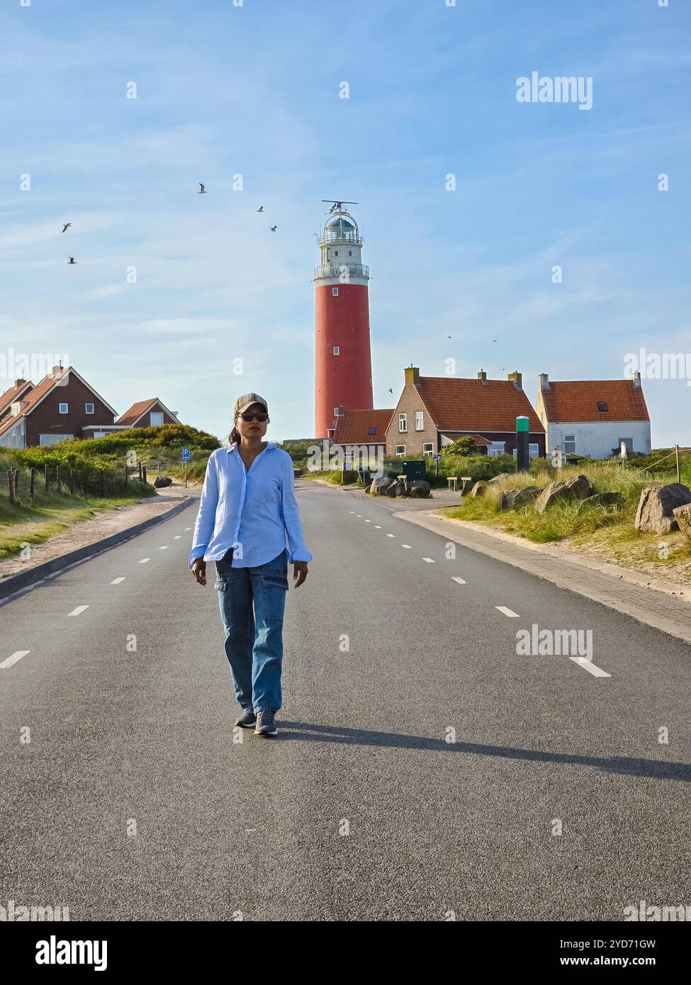 Un uomo solitario cammina lungo una strada vuota verso un faro distante a Texel, nei Paesi Bassi Foto Stock