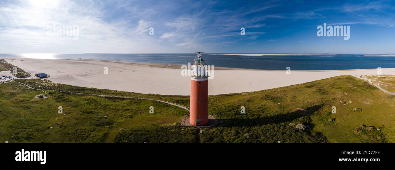 Una vista a volo d'uccello di un alto faro di Texel con un faro luminoso che splende su una spiaggia di sabbia, che si affaccia sul vasto oceano sulla i Foto Stock