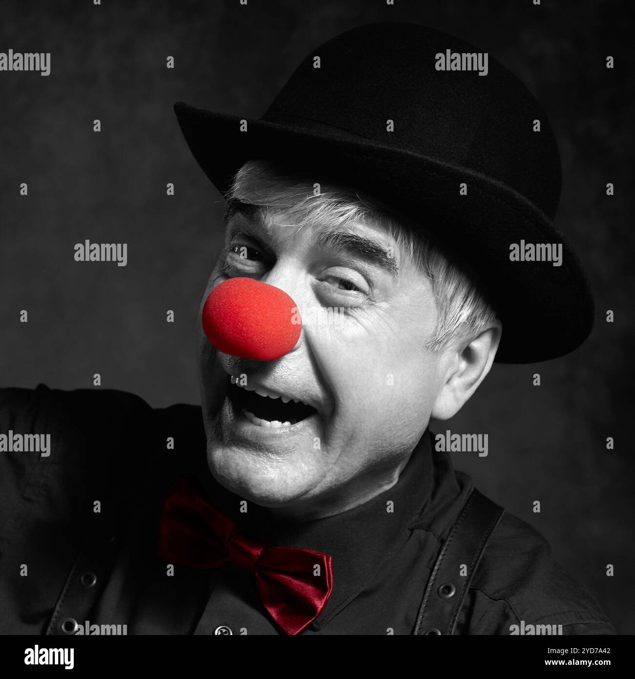 Ritratto a colori selettivo di clown ridendo. Vestito in camicia nera con bretelle, naso clown rosso e cappello bowler sulla testa Foto Stock