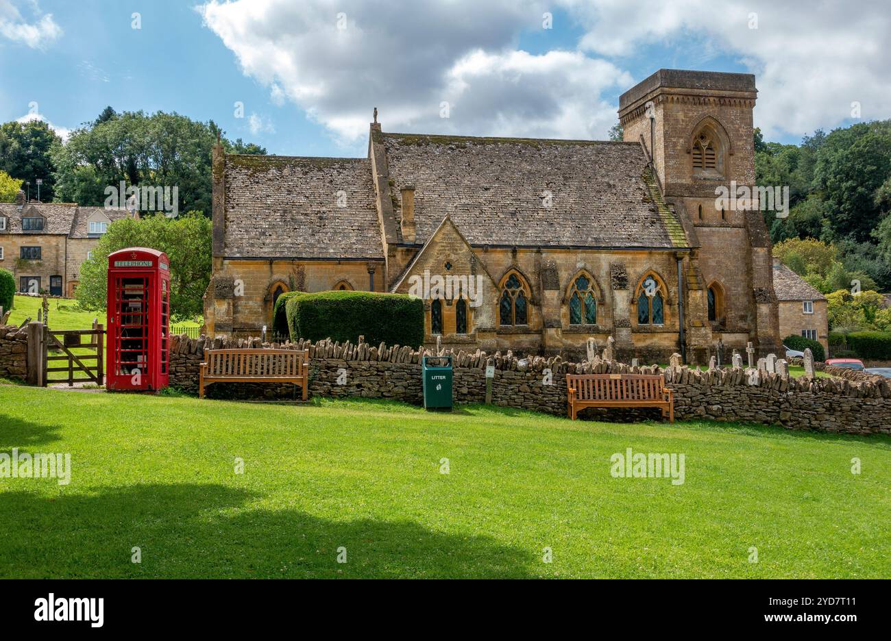 Un'incantevole vista del villaggio sulla chiesa di St. Barnabas a Snowshill con una classica cabina telefonica rossa annidata nel verde lussureggiante in una giornata di sole in Inghilterra Regno Unito Foto Stock