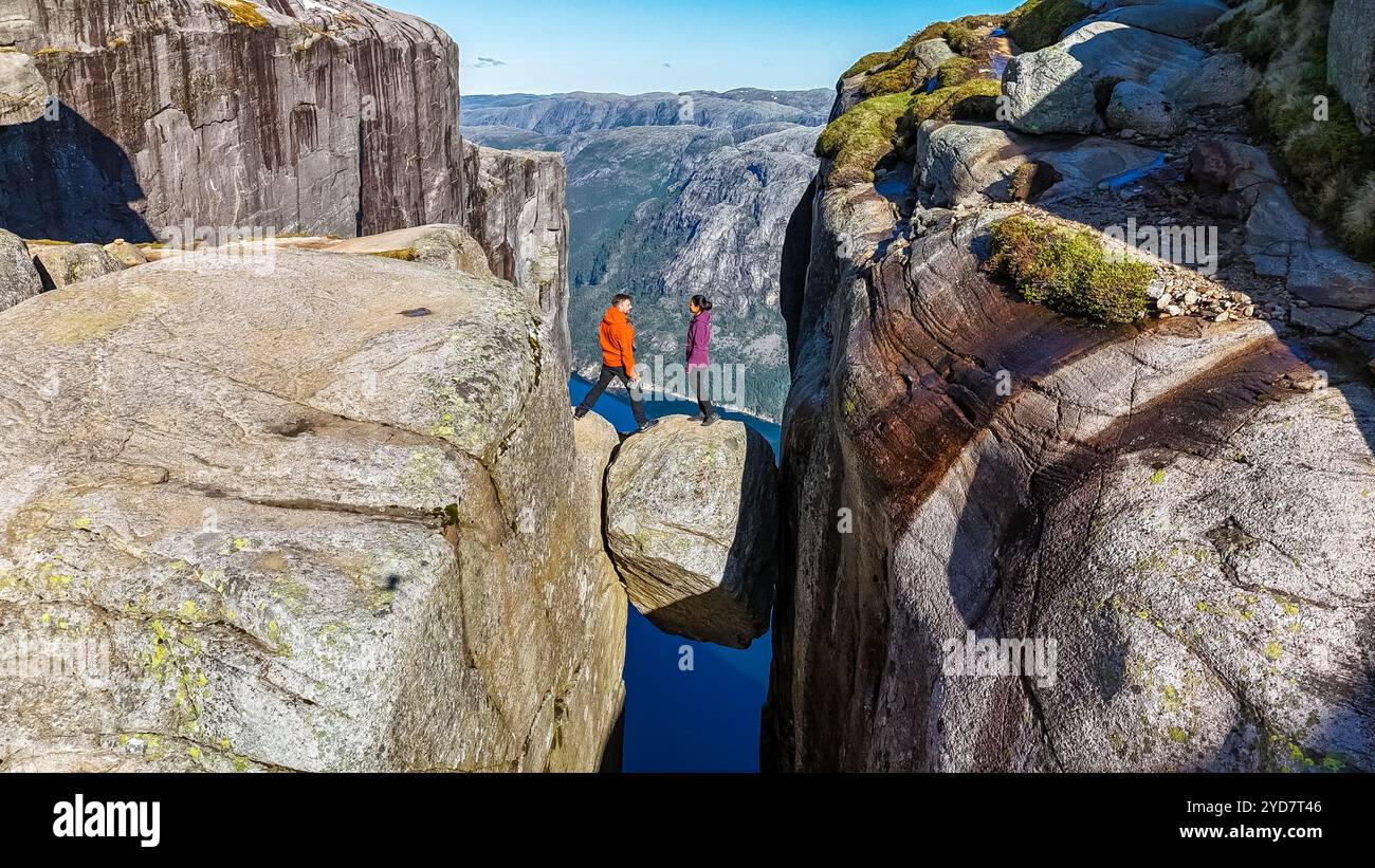 Due escursionisti si stagliano su una formazione rocciosa ai margini di Kjeragbolten, Norvegia, che si affaccia sulla vasta distesa sottostante Foto Stock