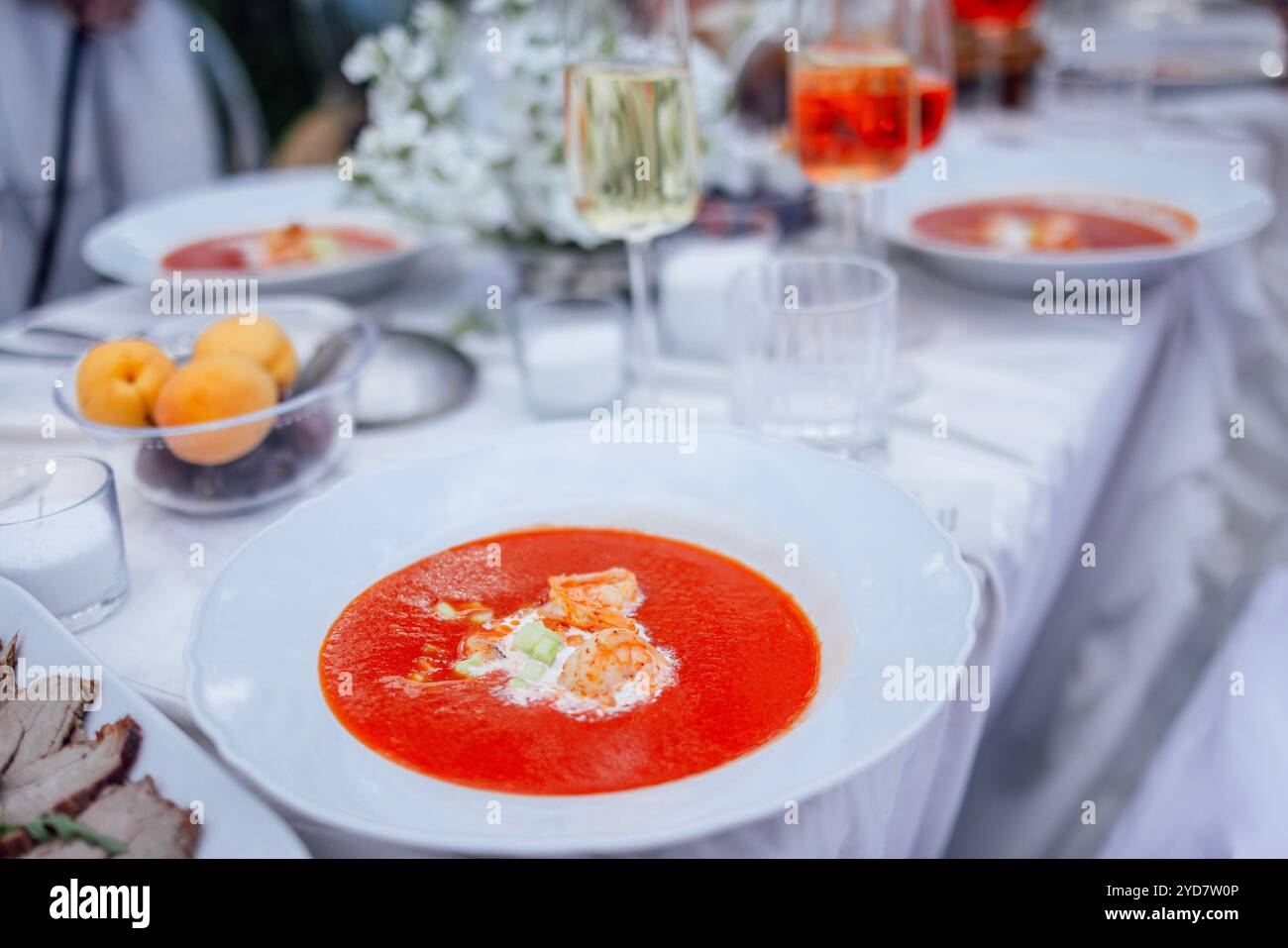 Primo piano di un piatto di gazpacho e di un tavolo festivo coperto con una tovaglia bianca. Deliziosa zuppa di pomodoro, bicchieri di vino e Foto Stock