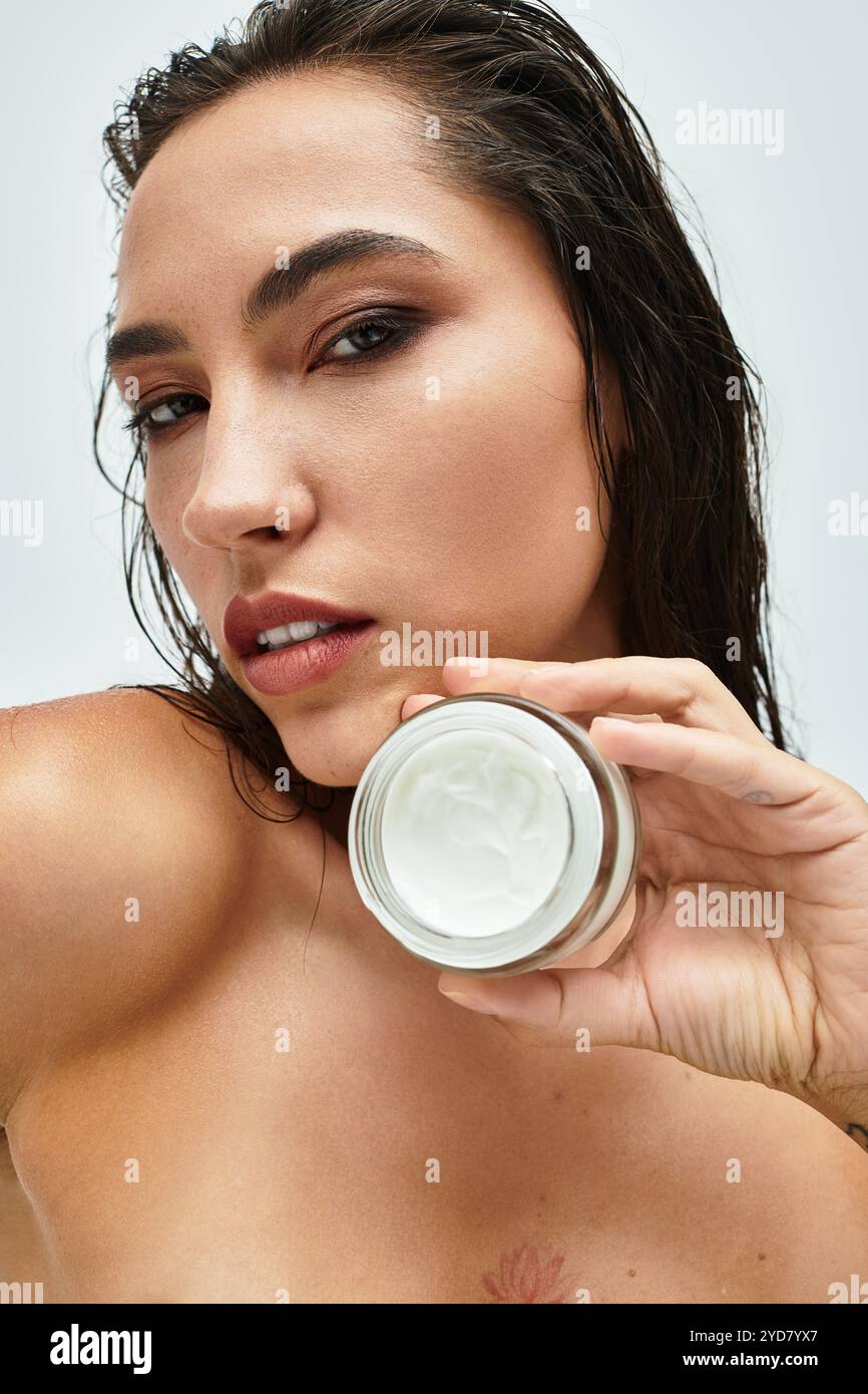 Questa splendida donna mette in risalto la sua pelle radiosa tenendo delicatamente in mano una crema nutriente. Foto Stock