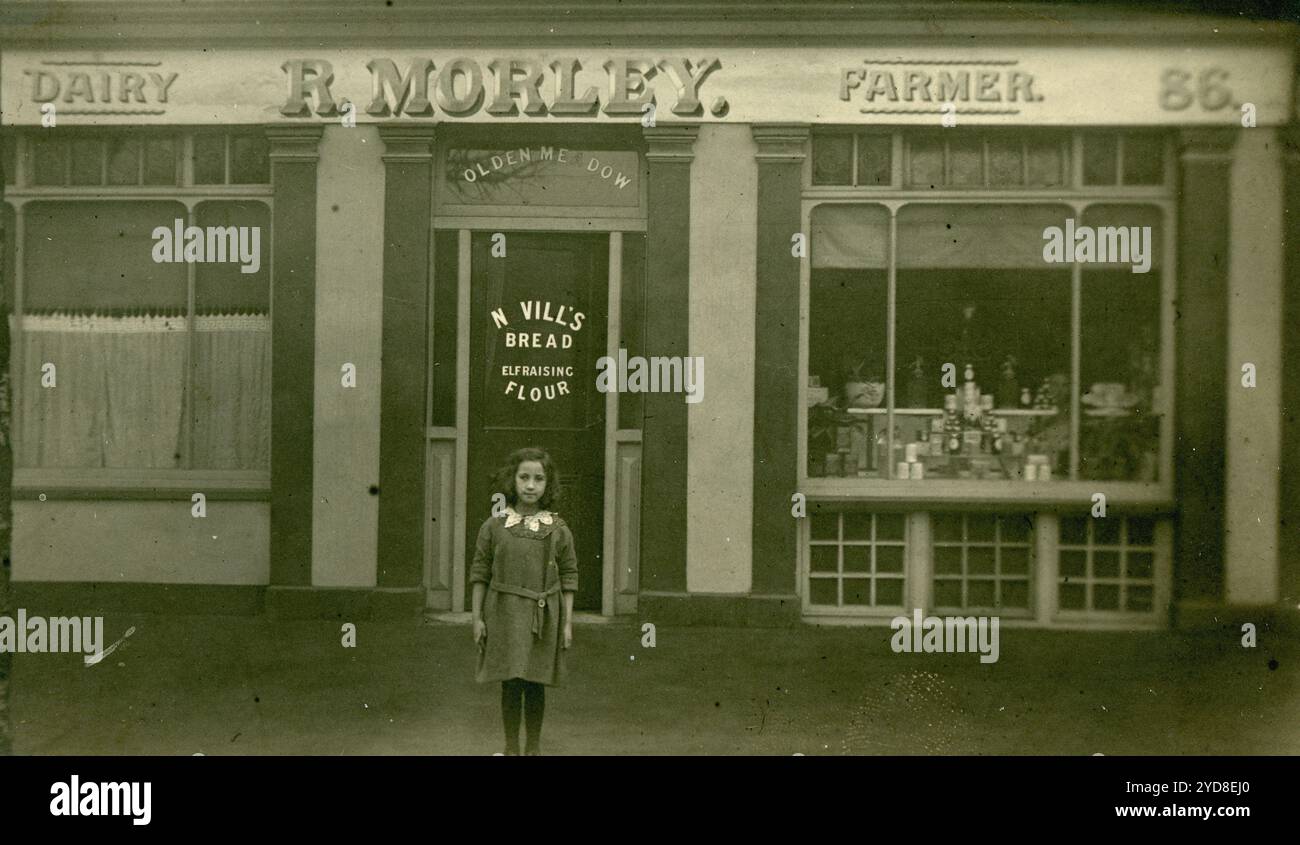 Cartolina originale dell'era della prima Guerra Mondiale di una bambina in piedi fuori in un negozio. R Morley, Dairy Farmer e' il segno del negozio. I locali del negozio di prodotti caseari erano al 86 di Richmond Road, Kingston, Surrey. Il cartello della vetrina pubblicizza il pane di Nevill. Circa 1913, Regno Unito Foto Stock