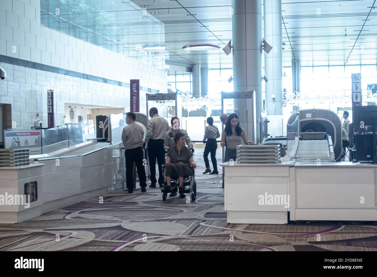 Un dipendente dell'aeroporto che assiste una donna su una sedia a rotelle, controllo di sicurezza del bagaglio a mano prima dell'ingresso del cancello, Aeroporto Changi di Singapore Foto Stock