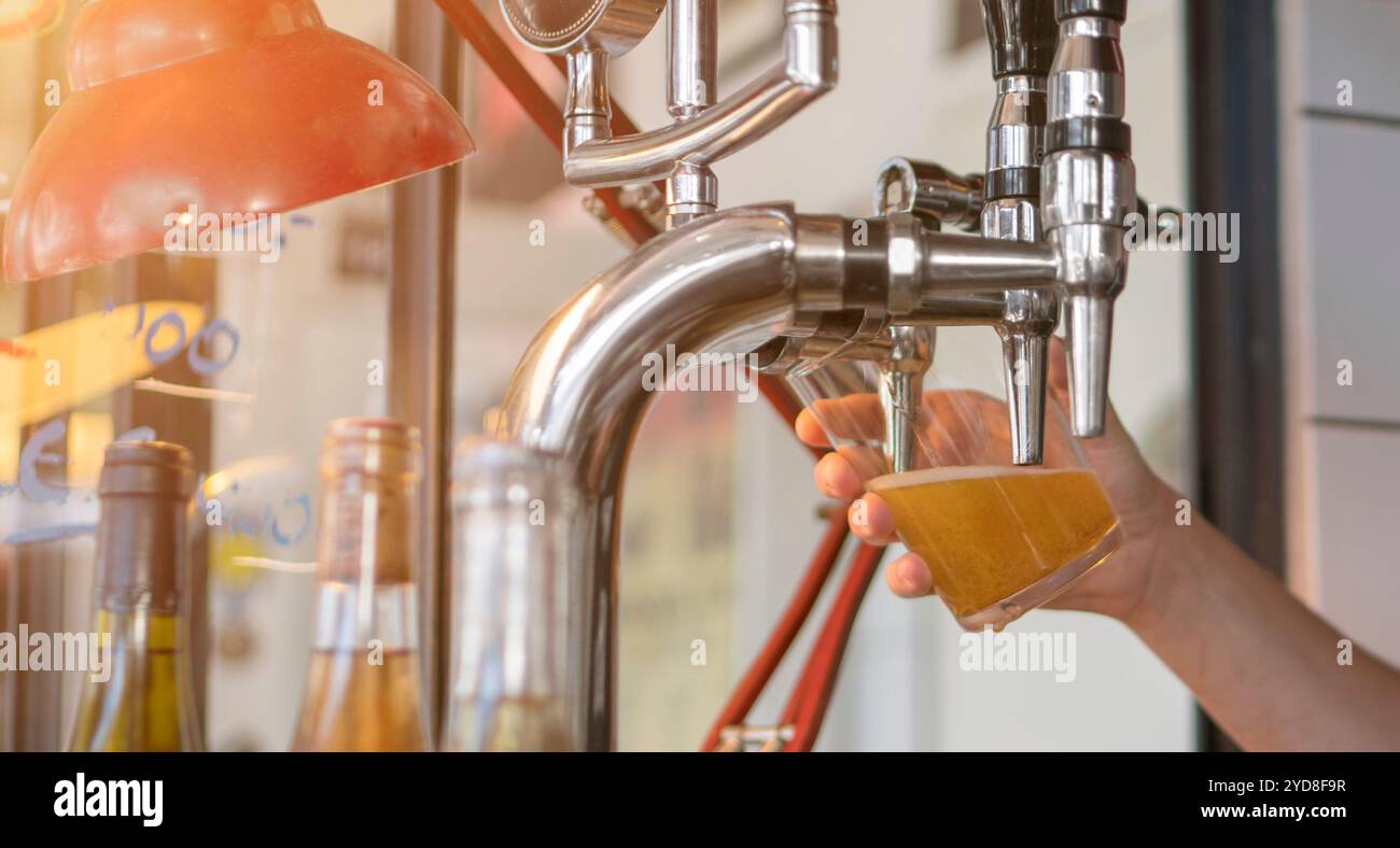 La birra fredda viene versata in un bicchiere dal barista dalla spillatura del pub. Immagine orizzontale di un bicchiere di birra al bar. Foto Stock