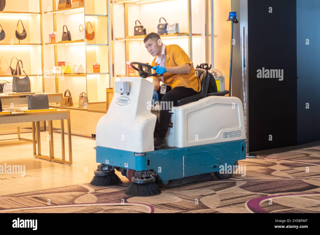 Un lavoratore della Tennant 6100 Sub-Compact Ride-On Sweeper pulisce tappeti nell'aeroporto Changi di Singapore Foto Stock