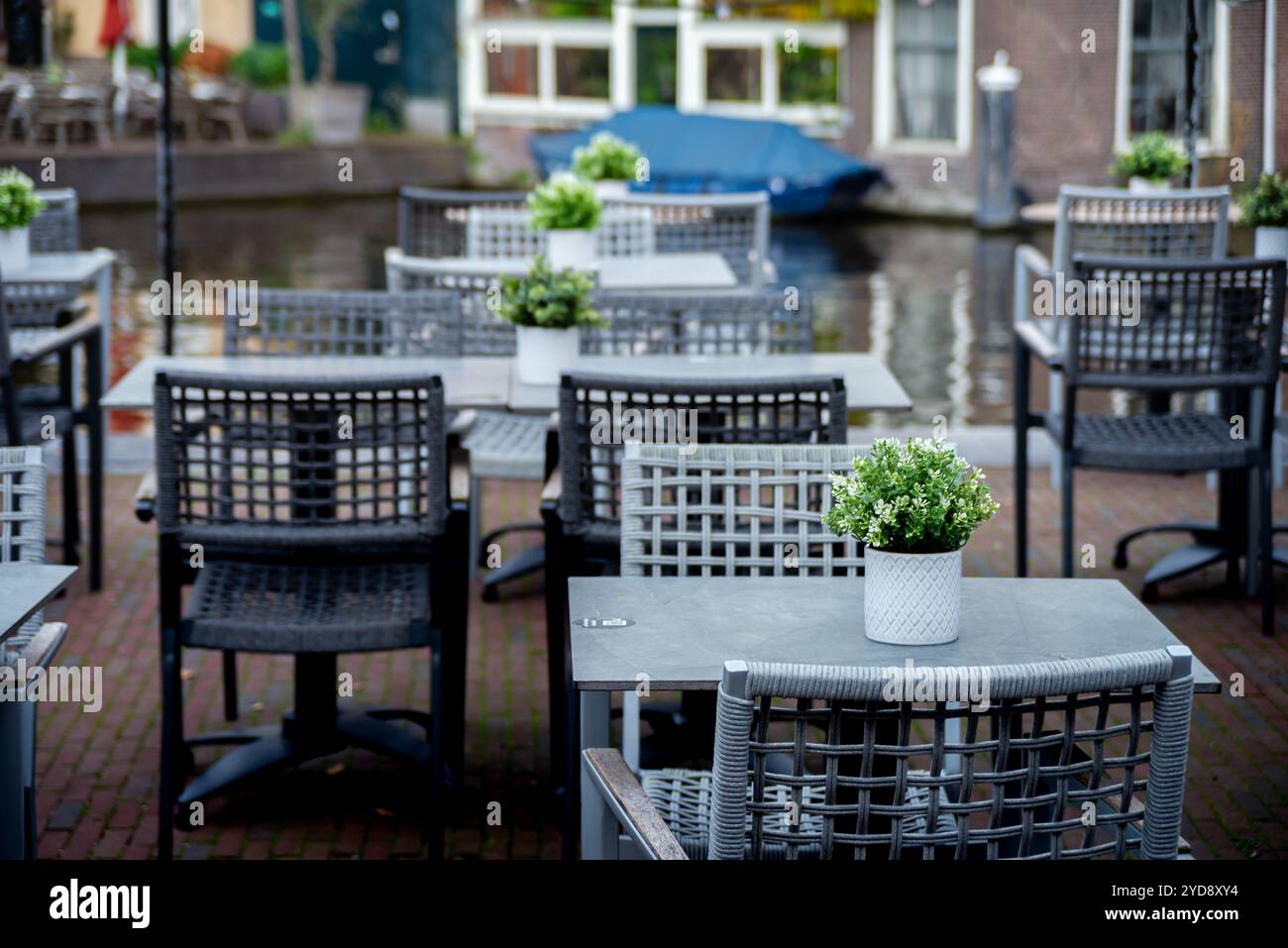 Una pittoresca caffetteria a Leida, Paesi Bassi, con posti a sedere all'aperto vicino a un canale, con tavoli bianchi e piante in vaso, sedie in vimini e una barca blu ormeggiata nelle vicinanze Foto Stock