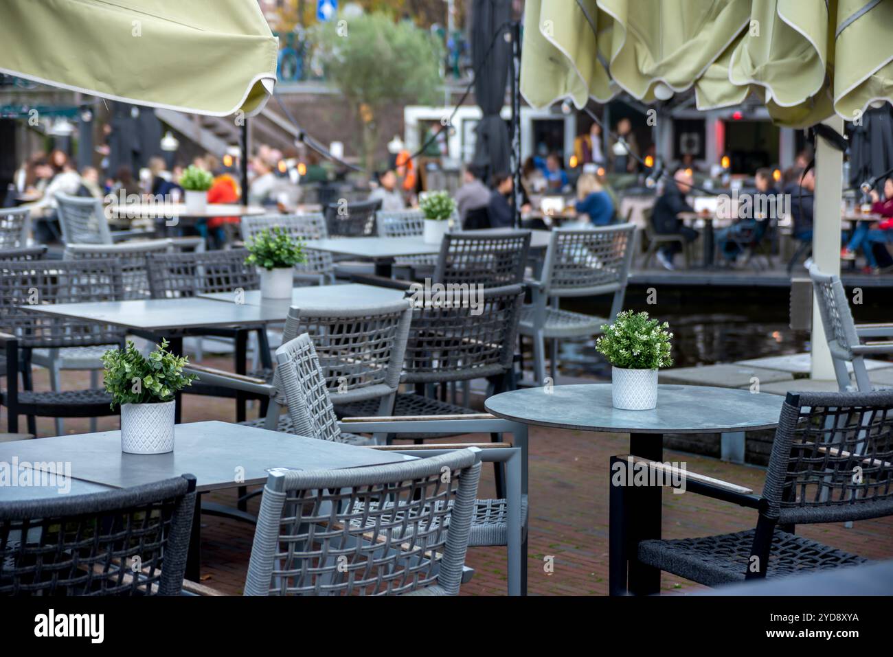 Un'affascinante caffetteria a Leida, Paesi Bassi, con posti a sedere all'aperto vicino a un canale. Tavoli bianchi con piante in vaso, sedie in vimini, leiden, paesi bassi Foto Stock