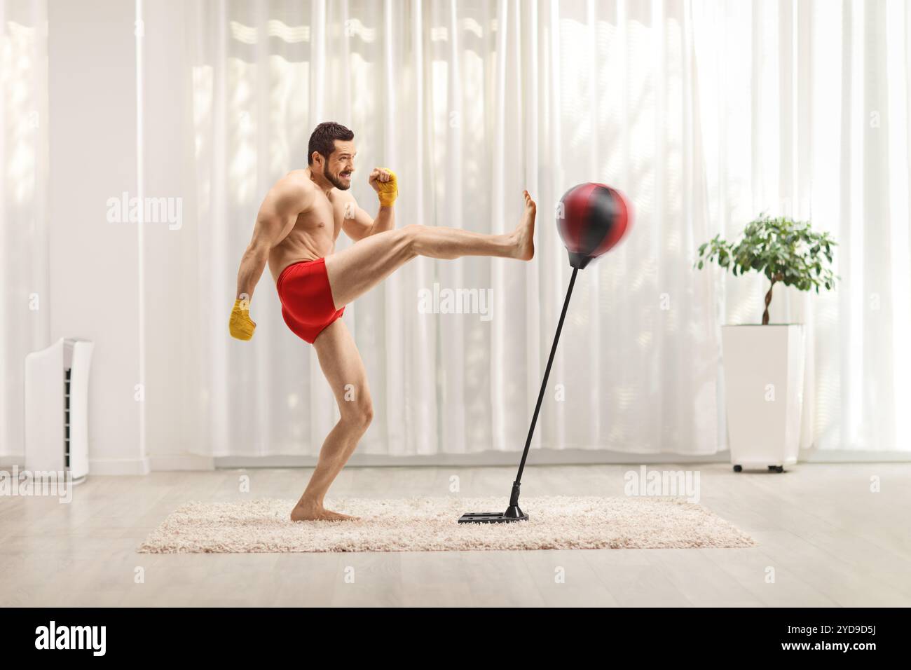 Foto a tutta lunghezza di un uomo in forma che si esercita con il kickboxing con un supporto per pugni in una stanza Foto Stock