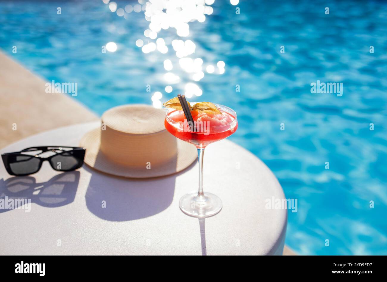 Una bevanda rossa in un elegante bicchiere con gambo lungo sul lato della piscina. Foto Stock