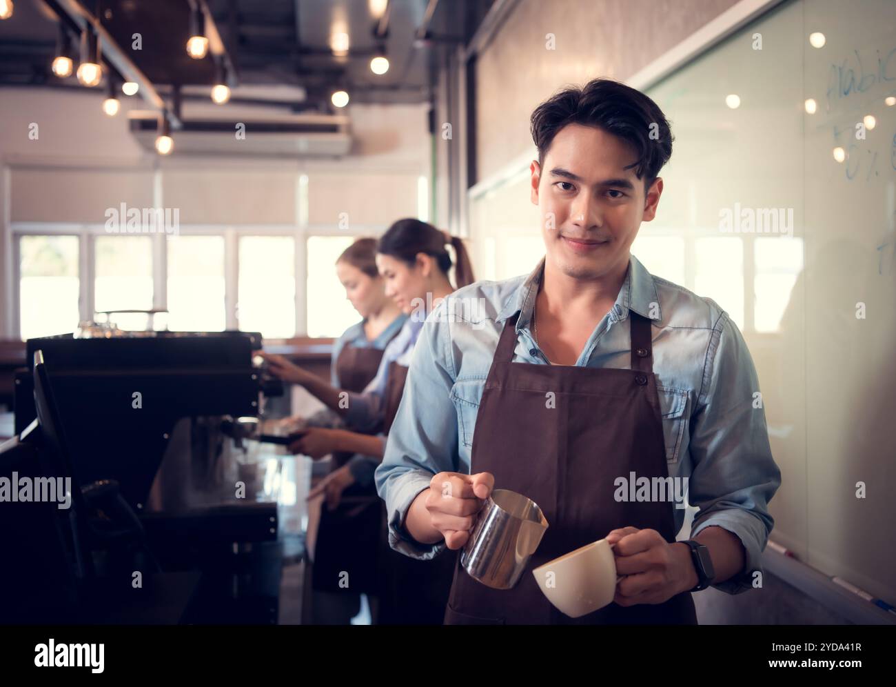 Giovane barista esperto nella preparazione del caffè campione, creando latte art in una tazza di caffè per un cliente. Foto Stock