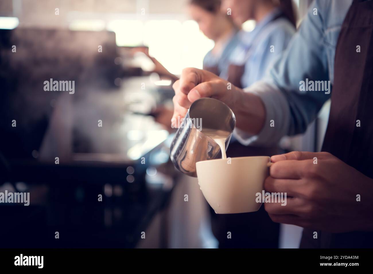 Giovane barista esperto nella preparazione del caffè campione, creando latte art in una tazza di caffè per un cliente. Foto Stock