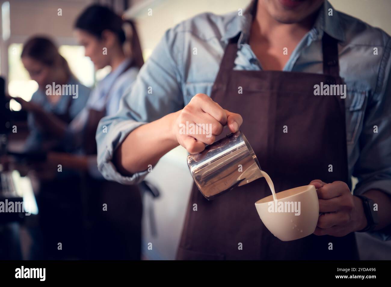 Giovane barista esperto nella preparazione del caffè campione, creando latte art in una tazza di caffè per un cliente. Foto Stock