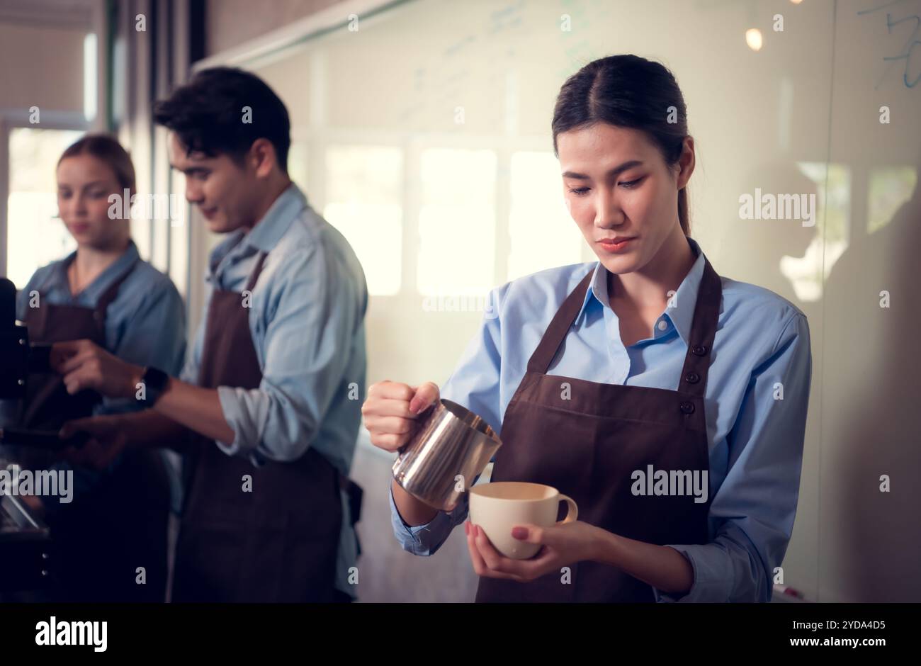 Una giovane barista esperta nella produzione di caffè Champion, che crea latte art in una tazza di caffè per un cliente. Foto Stock
