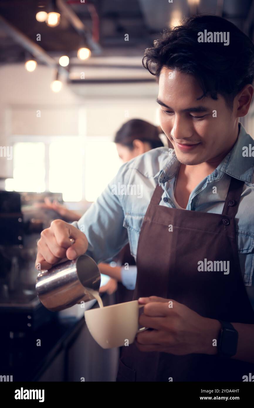 Giovane barista esperto nella preparazione del caffè campione, creando latte art in una tazza di caffè per un cliente. Foto Stock