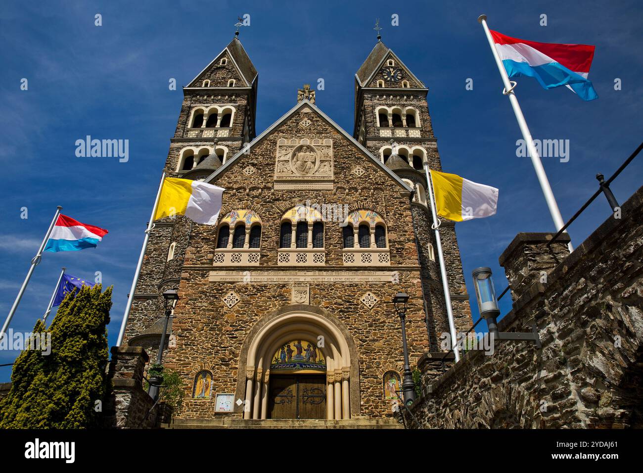 Roemisch-katholische Pfarrkirche in Clerf mit Kirchenfahne und Luxemburgischer Fahne, Herzogtum Luxemburg, Europa Foto Stock